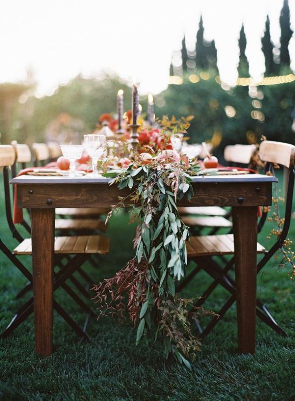 A fall wedding table runner with olive greenery, dried greenery and foliage and pomegranates and other fruits