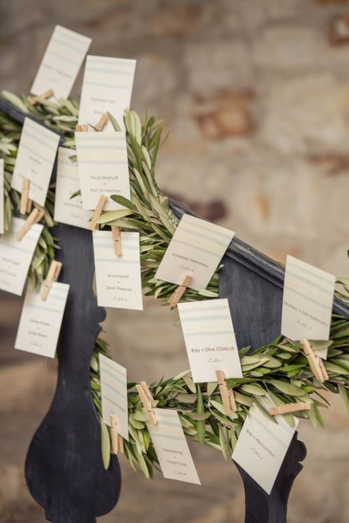 a wedding seating chart with olive greenery, cards and clothespins is a simple and rustic idea for a modern wedding