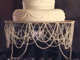 a white pearl wedding cake with pink blooms and pearl strands covering the wedding cake stand to present the cake at its best