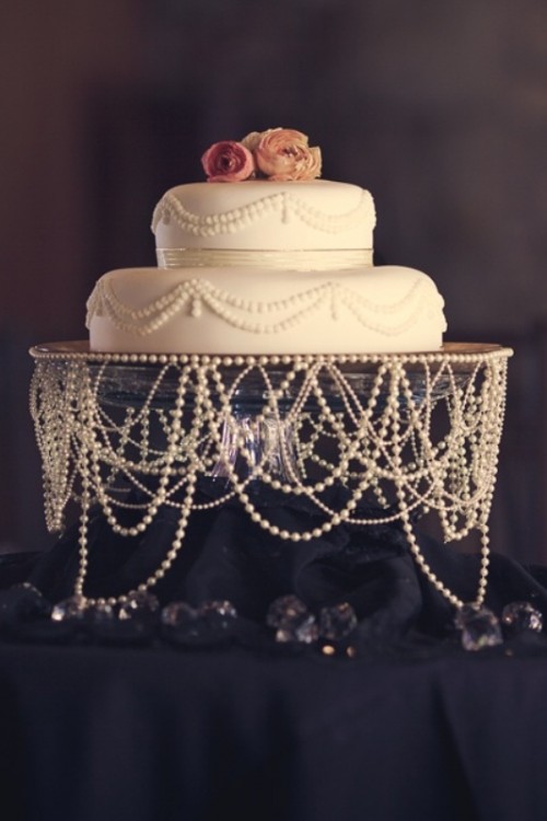 a white pearl wedding cake with pink blooms and pearl strands covering the wedding cake stand to present the cake at its best