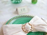 an elegant place setting with a green charger, a plate with a beaded edge and a large napkin bow with a pearl buckle