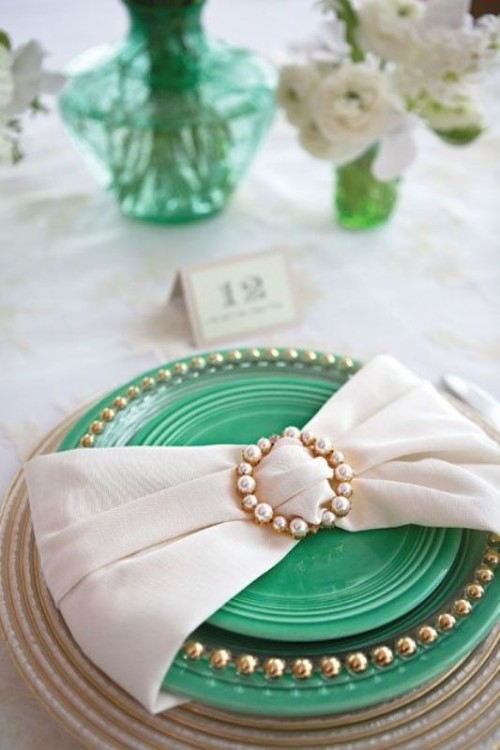 an elegant place setting with a green charger, a plate with a beaded edge and a large napkin bow with a pearl buckle