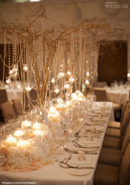 a statement centerpiece of branches with lots of pearls and crystals and candleholders hanging on them