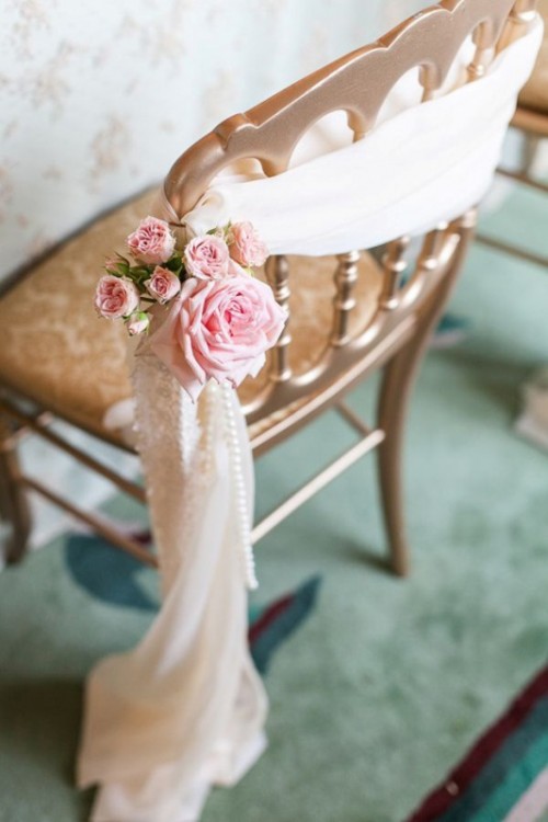 a wedding chair covered with fabric, pink blooms and pearls is a creative take on wedding signage that you usually see