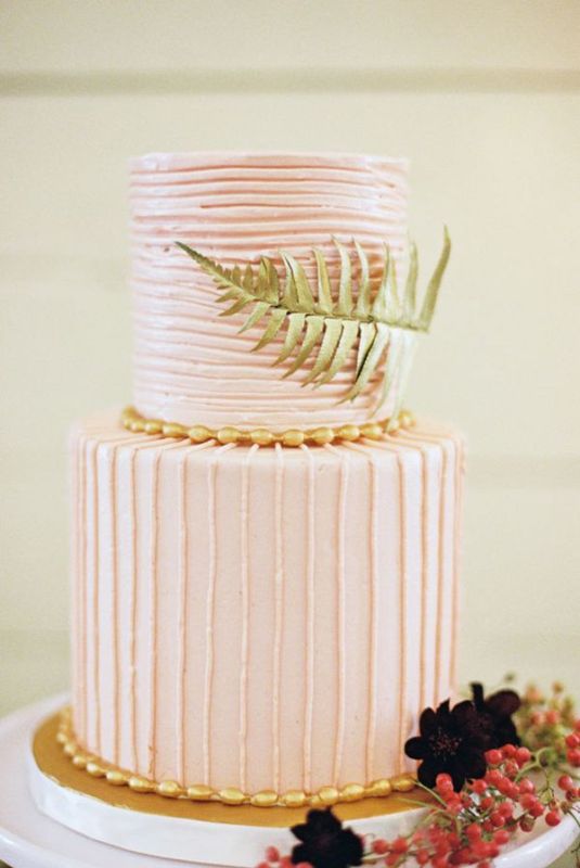 A striped light pink wedding cake with horizontal and vertical stripes, with a large fern leaf is a lovely idea for a tropical wedding