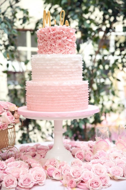 a light pink wedding cake with two ombre tiers, with a pink floral tier, gold monogram toppers is a gorgeous idea for a wedding