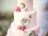 a light pink wedding cake with pink real blooms, grey sugar ones and vintage brooches, with a doily on top and some pink blooms added