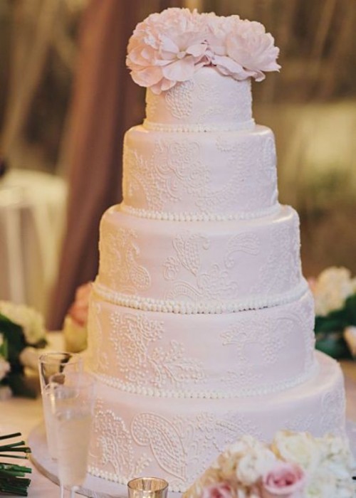 a light pink wedding cake with lovely white patterns, with pink sugar blooms on top for a super refined and stylish spring or summer wedding