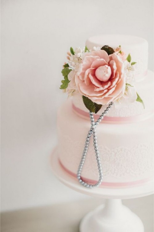 a light pink wedding cake with mauve ribbons and white doilies, fresh and sugar blooms and pearls for a chic and lovely look