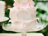 a unique wedding cake covered with light pink petals, with pink sugar blooms and green leaves is a lovely idea for a fun and cool spring or summer wedding