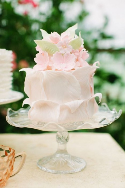 a unique wedding cake covered with light pink petals, with pink sugar blooms and green leaves is a lovely idea for a fun and cool spring or summer wedding