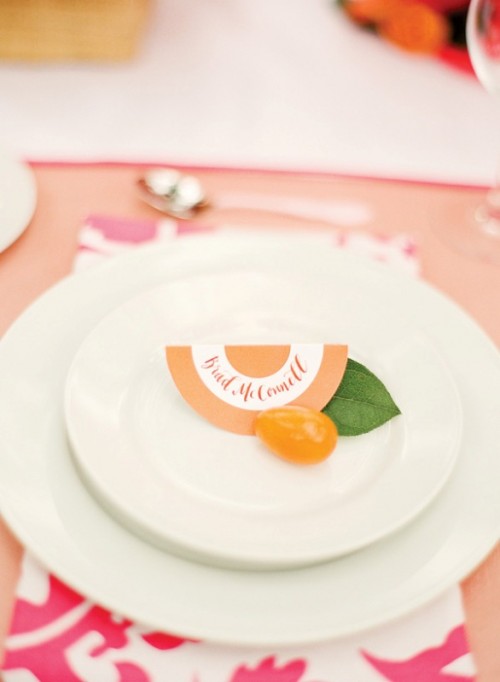 a bright wedding place setting with a peachy tablecloth, white porcelain, a printed napkin and kumquat for a touch of color
