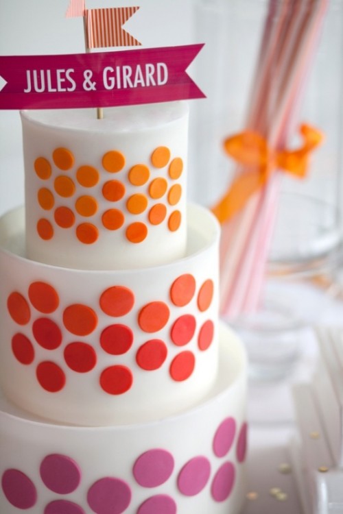 a white wedding cake decorated with colorful polka dots and a couple of flags on top is a bold and colorful idea for a modern wedding