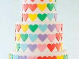 a white wedding cake covered with colorful hearts is a fun and cool idea for a bright and colorful wedding