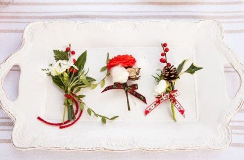 Cool green, white and red boutonnieres with leaves, pinecones, cotton and wood slices and bright ribbons