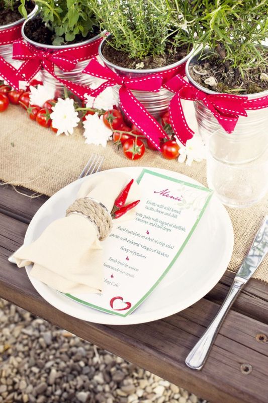 A winter or Christmas wedding tablescape dotted with red and grene touches, with potted herbs and menus and napkins