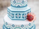 a light blue wedding cake with bolder blue, grey patterns, bright blooms, succulents nad a pincushion protea is a lovely and bright idea for a Mediterranean wedding