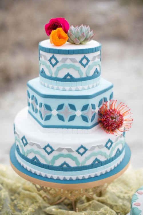 a light blue wedding cake with bolder blue, grey patterns, bright blooms, succulents nad a pincushion protea is a lovely and bright idea for a Mediterranean wedding