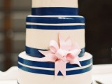 a white wedding cake with navy stripes and a a pink sugar ribbon bow for a nautical wedding