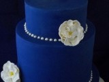 an electric blue wedding cake decorated with white sugar blooms and white pearls all over the cake for an elegant wedding with royal blues