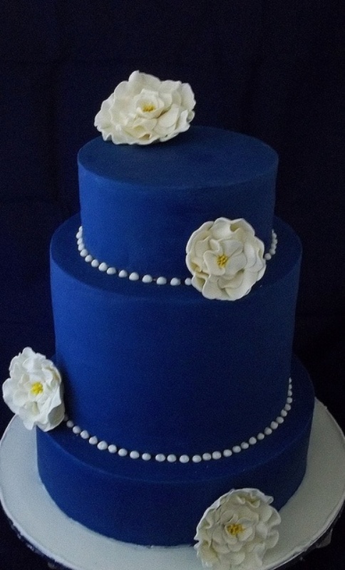an electric blue wedding cake decorated with white sugar blooms and white pearls all over the cake for an elegant wedding with royal blues