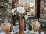 a rustic wedding centerpiece with moss, ranunculus, wheat and fresh and dried blooms plus a stack of books