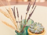 a simple rustic wedding centerpiece of a potted succulent, lavender and wheat and a green glass is a lovely decoration to rock