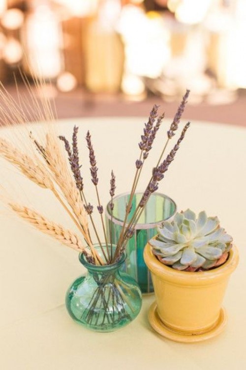 a simple rustic wedding centerpiece of a potted succulent, lavender and wheat and a green glass is a lovely decoration to rock
