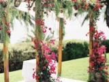 a colorful tropical wedding arch covered with greenery and fuchsia blooms will make a statement with color