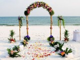 a bright tropical wedding arch covered with greenery and super colorful blooms and with matching arrangements around