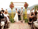a bamboo wedding arch decorated with bright blooms is a cool and classic tropical decor idea