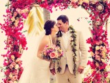 a super bright tropical wedding arch fully covered with bold blooms in fuchsia and pink shades