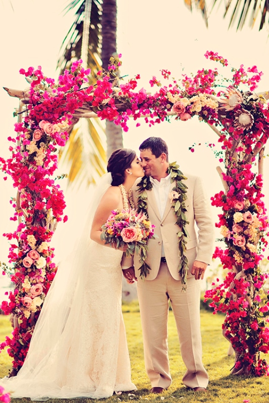 A super bright tropical wedding arch fully covered with bold blooms in fuchsia and pink shades