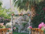 a wooden wedding arch decorated with greenery and bright flowers is a cool decoration with much color