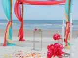 a super bright wedding ceremony space with a colorful wedding arch with turquoise and red fabric, bright blooms and petals