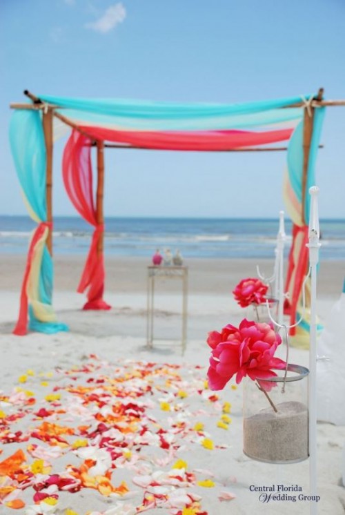 a super bright wedding ceremony space with a colorful wedding arch with turquoise and red fabric, bright blooms and petals