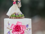 a handpainted one tier wedding cake with a fun topper on a wood slice with moss