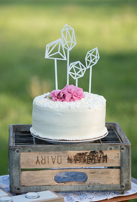 A white buttercream wedding cake topped with fresh pink blooms and with geometric toppers