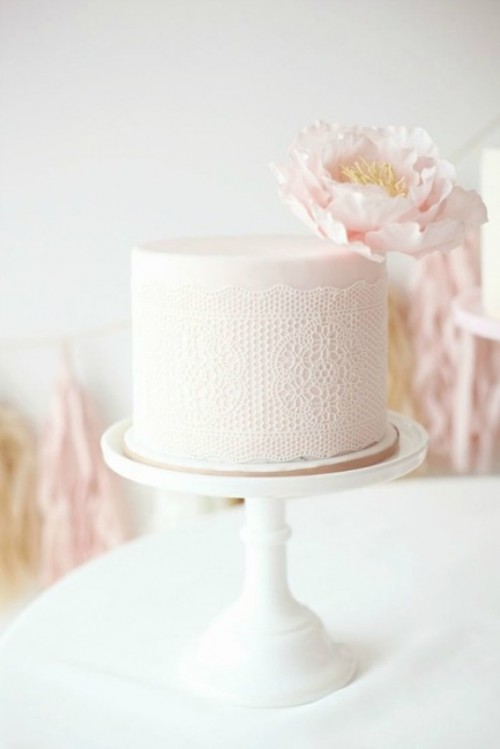 a blush wedding cake with lace decor and a single blush bloom on top is a very subtle and tender option