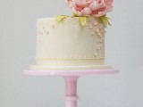 a neutral buttercream wedding cake decorated with pink sugar blooms and a fresh pink peony on top feels romance and vintage