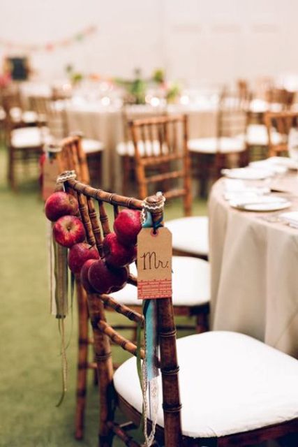 a red apple garland with ribbons is a lovely idea for wedding chairs decor, you can DIY as many as you want