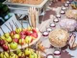 a fall wedding dessert table with pillar candles, apples on sticks and nuts and various toppings plus various dips