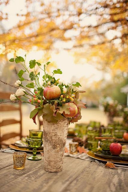 a rustic wedding centerpiece of a vase wrapped with bark, white blooms, greenery and apples is a cool piece to easily DIY