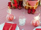a colorful rustic wedding tablescape with a plaid tablecloth and red napkins, packed apples as wedding favors and a wooden basket with them as part of a wedding centerpiece