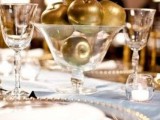 a stylish and elegant wedding tablescape with gold chargers and gold apples in a clear glass bowl as a centerpiece