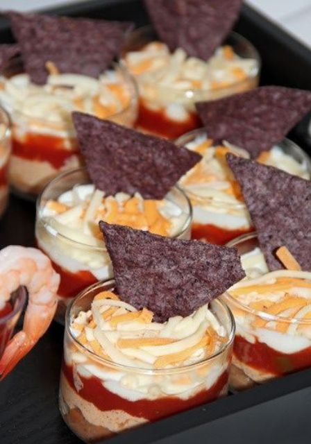 a layered appetizer with cream cheese, veggies, meat souffle and nachos on top