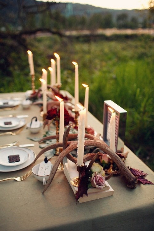 a fall woodland wedding tablescape with pink blooms, fall leaves, antlers and tall and thin candles, gold cutlery and neutral linens is awesome