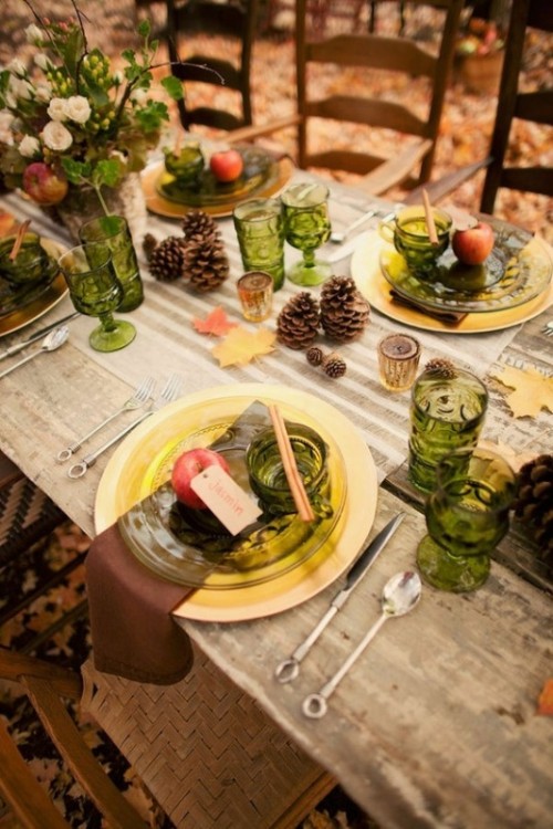 a gorgeous woodland fall wedding tablescape with a striped runner, brown napkins, gold and yellow chargers and plates, green glasses, greenery, pinecones, apples and neutral blooms