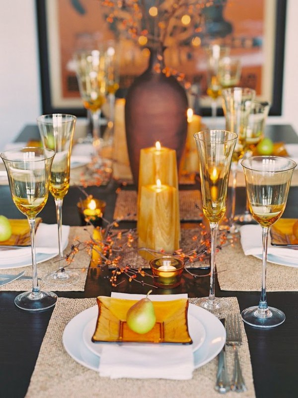A rust and orange fall wedding tablescape with amber chargers, amber glasses, candles, some faux branches with sparkles and a large vase with them