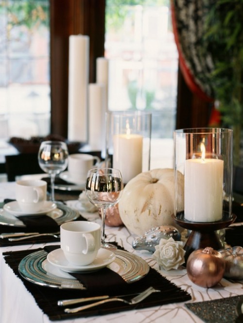 a black and white fall wedding tablescape with white pillar candles, white and metallic pumpkins, black placemats, silver chargers and cutlery and blooms is cool